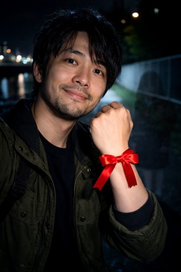 金子一輝 手首に赤いリボンを付けた自撮り写真 背後にうっすらとランドセルを背負った少女が映っている